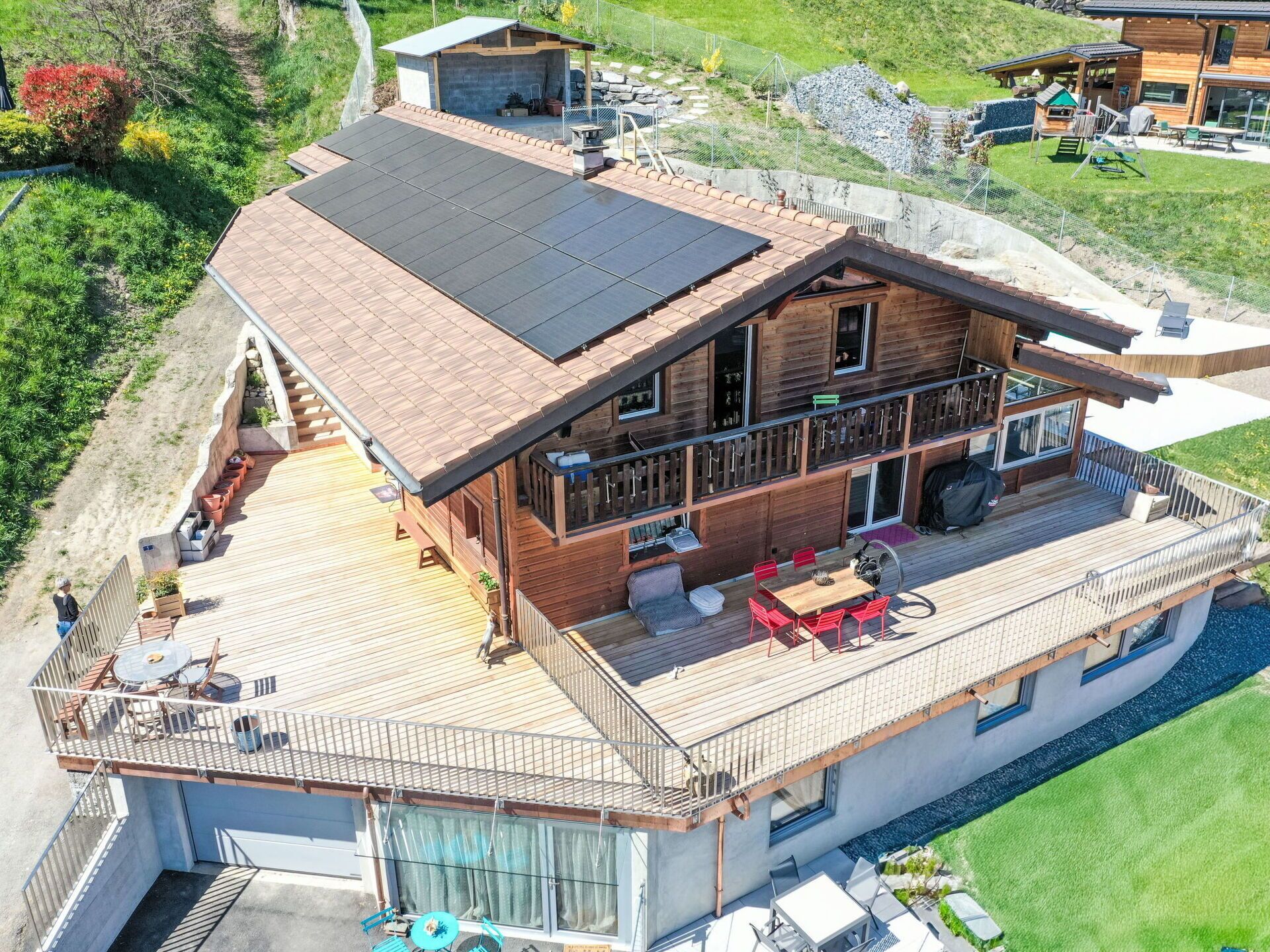 A two-story wooden house with a balcony, outdoor seating, and a swimming pool.
