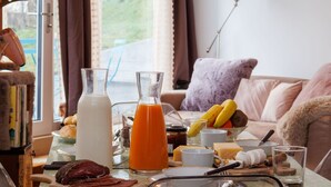 Una mesa de desayuno con diferentes alimentos, una jarra de leche y un vaso de zumo de naranja.