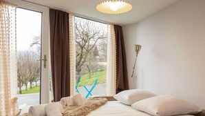Un dormitorio con cama, una manta suave y vistas a un parque a través de amplios ventanales.