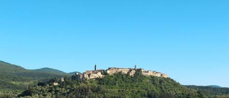A historic hilltop town with ancient buildings, surrounded by dense forest and hills.
