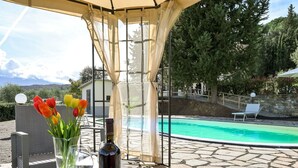A covered outdoor area with a pool, a table with a bottle and glass, and a vase with tulips. - Wonderful private villa with private pool, WIFI, TV, patio, pets allowed and panoramic view (Castel Del Piano)