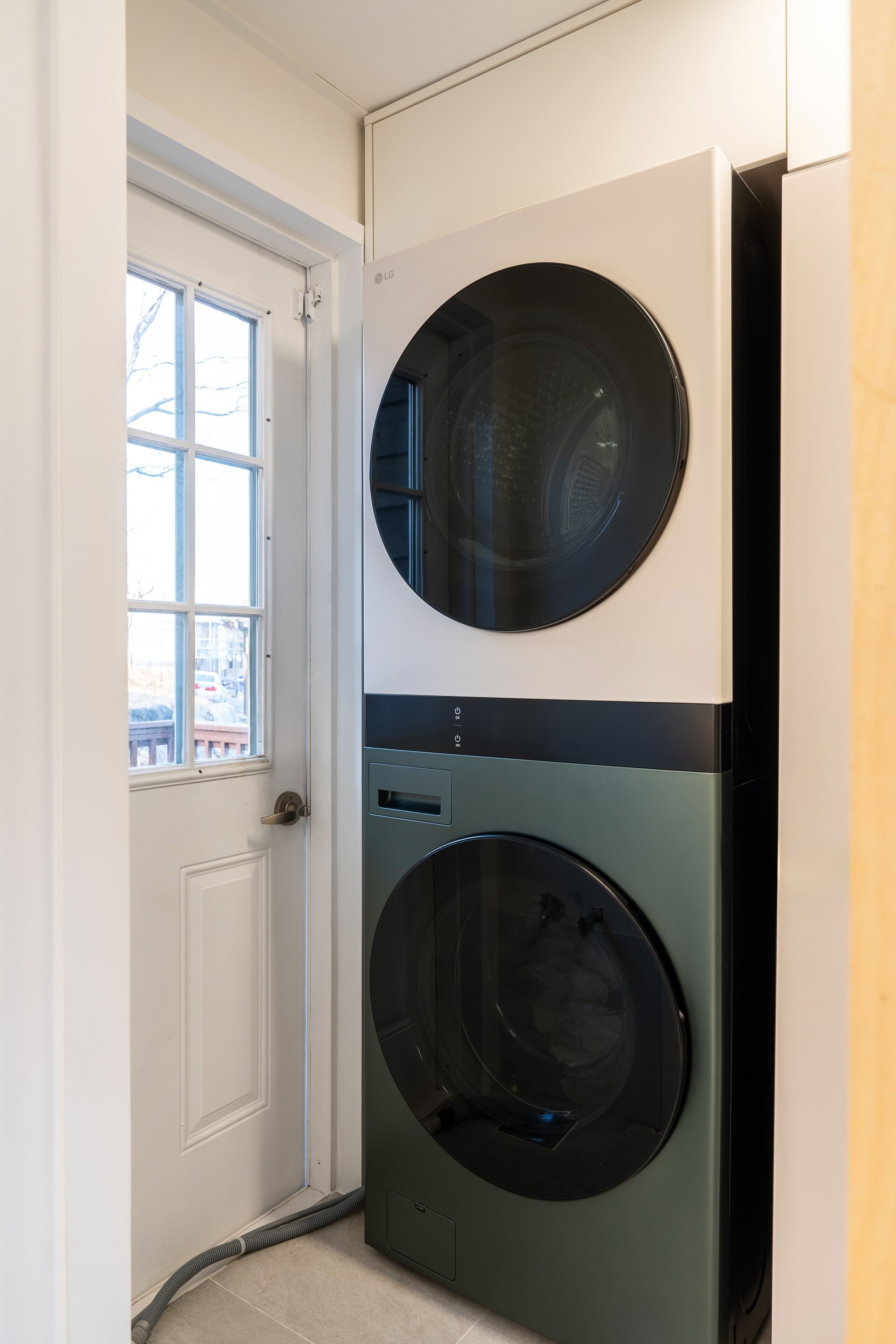 A laundry room with two stacked washing machines, a door, and a window.