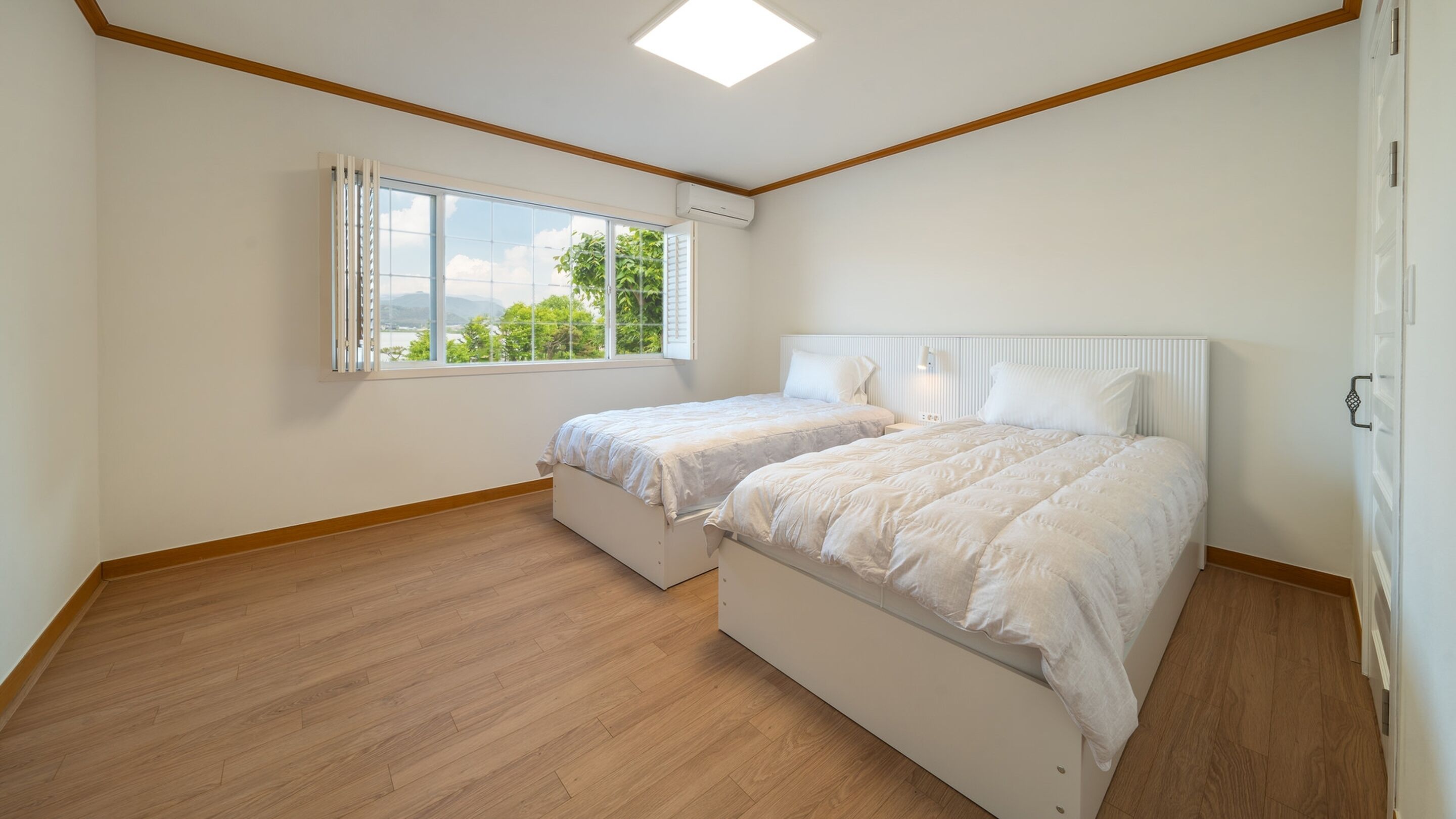 Une chambre avec deux lits, une fenêtre donnant sur un beau paysage et un luminaire au plafond.