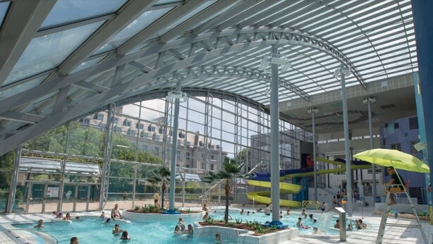 Una piscina interior con múltiples carriles, una zona cubierta y vistas a edificios cercanos.