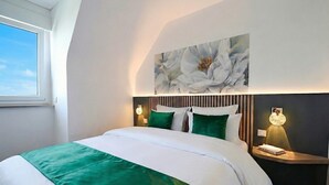 Habitación de hotel moderna con una cama grande, ropa de cama verde, una obra de arte en la pared y lámparas de noche.