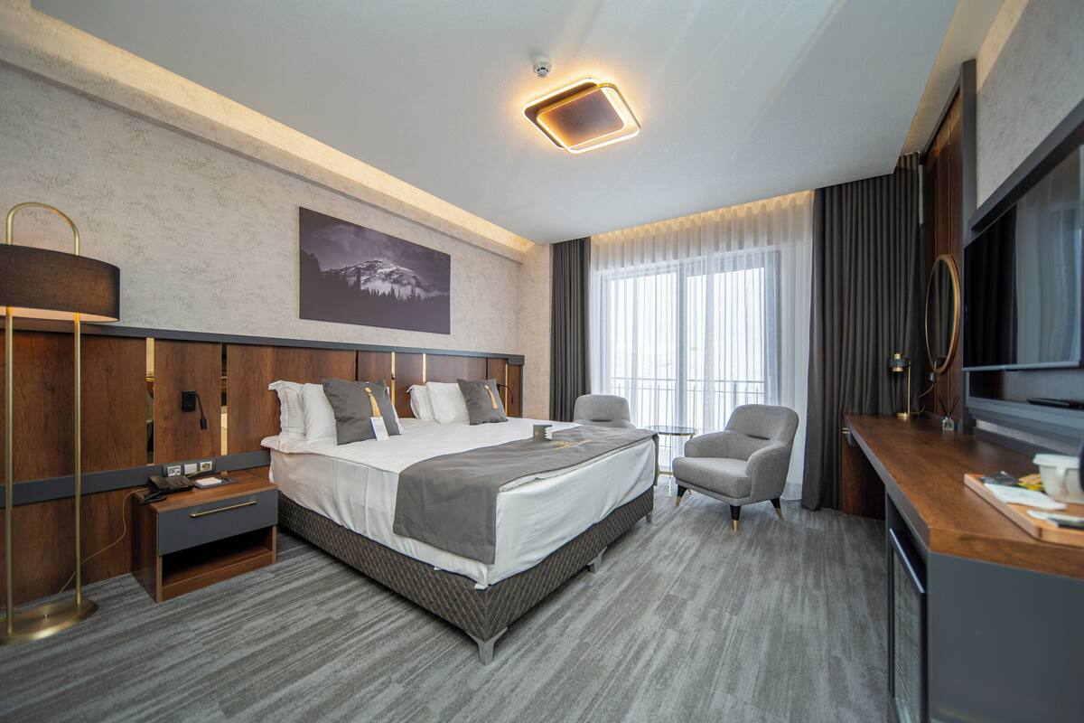 Quarto de hotel moderno com uma cama grande, uma escrivaninha, uma cadeira e uma televisão.