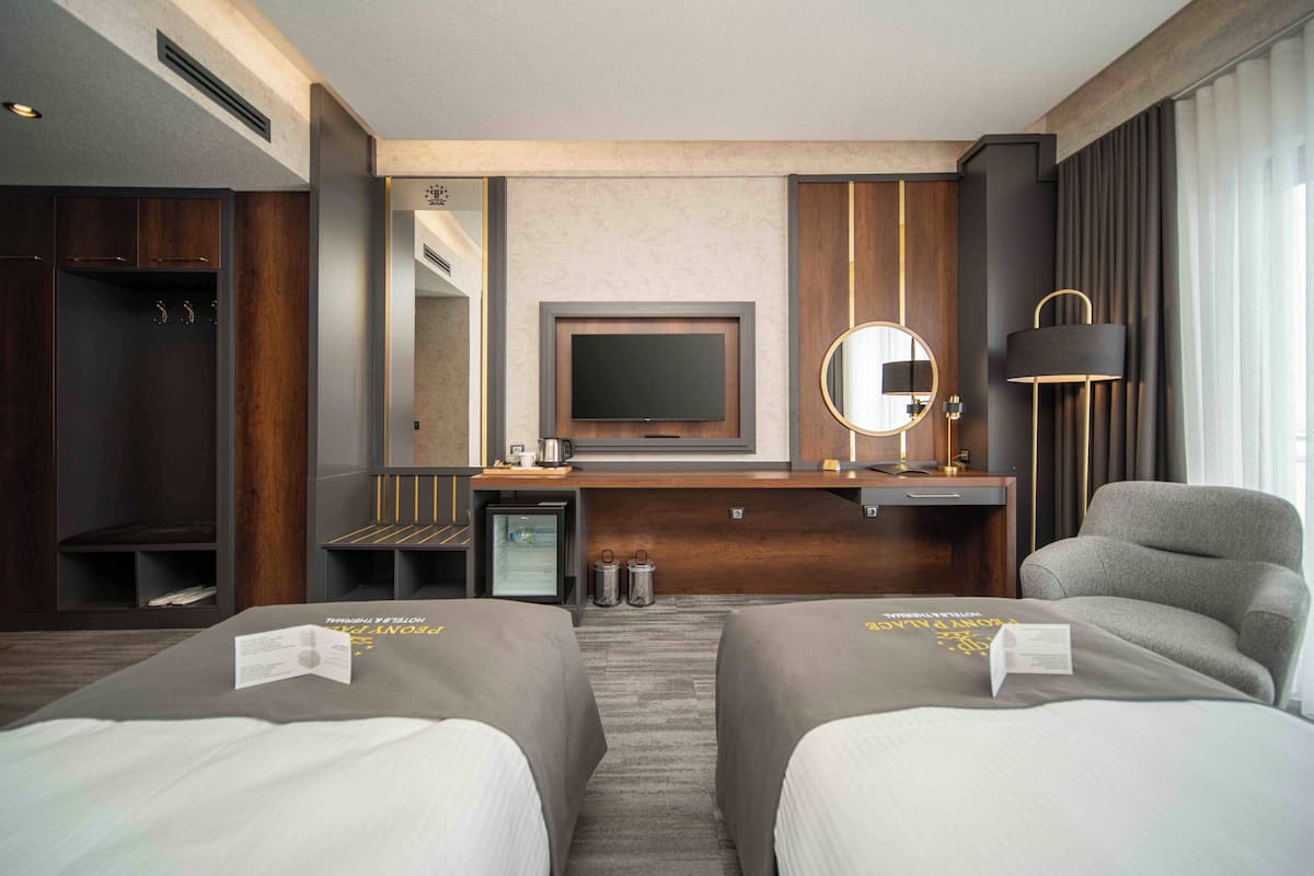 Quarto de hotel com duas camas, televisão, escrivaninha, cadeira e armário.