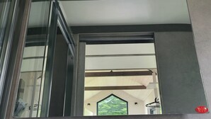 Een modern interieur met een glazen liften deur, een plafond met inbouwverlichting en uitzicht op een groen landschap door een raam.