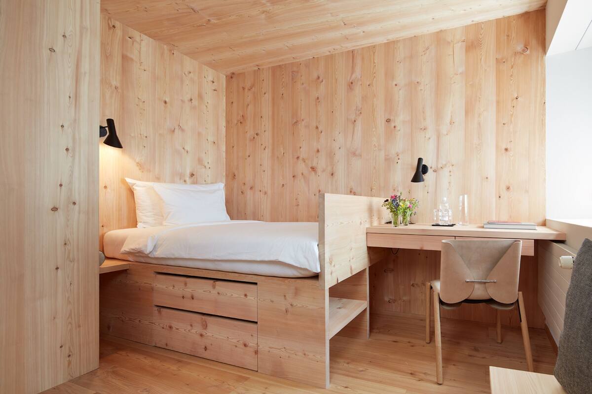 A wooden room with a bed, desk, and chair.