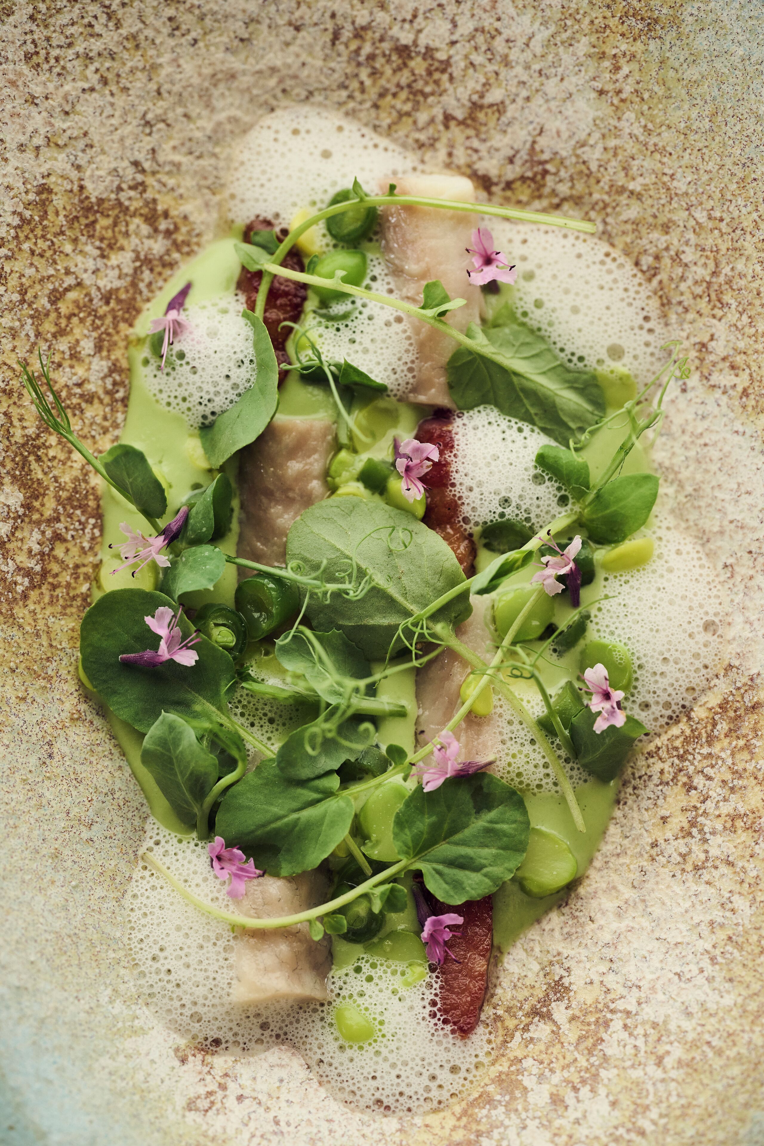 A dish with greens and pink flowers on a textured surface.