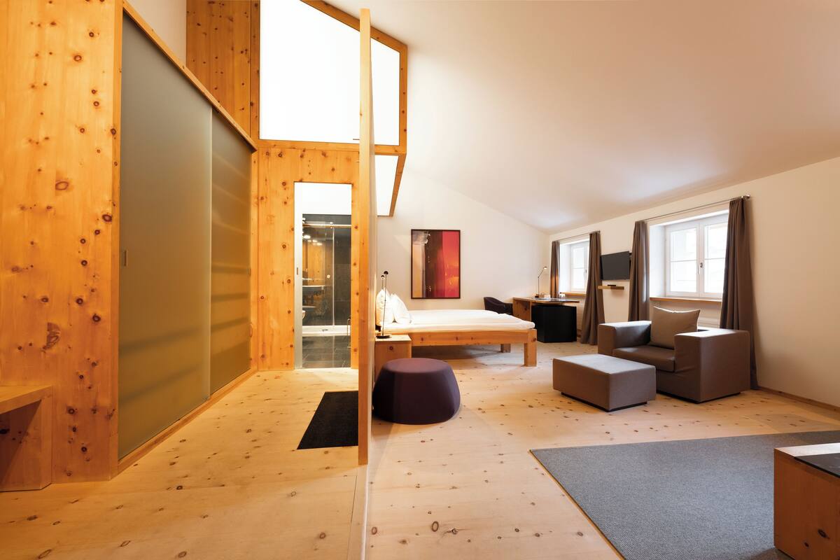 A modern, well-lit room with a wooden floor, a bed, a sofa, and a small table.