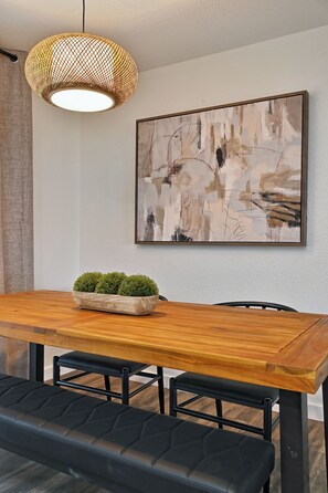 A dining area with a wooden table, black cushioned bench, and a woven pendant light. - Escape to Manor Hill Haven! Accessible 2BR retreat with hot tub, modern comfort & mountain views. Perfect for families, couples & business travelers. (Medford)