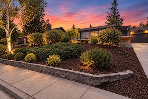 A modern residential property with a landscaped garden, a stone retaining wall, and a garage.