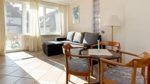 A living room with a sofa, a small table, and two chairs. There is a window with curtains, a radiator, and a lamp. - Holiday Studio in Rewal, Breakfast Included (Rewal)