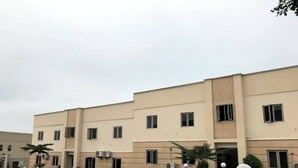 A multi-story building with a beige facade, multiple windows, and air conditioning units. There are parked cars and a green trash bin in the foreground.