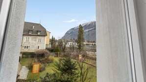 A view from a window of a residential area with houses, a garden, and mountains in the background.