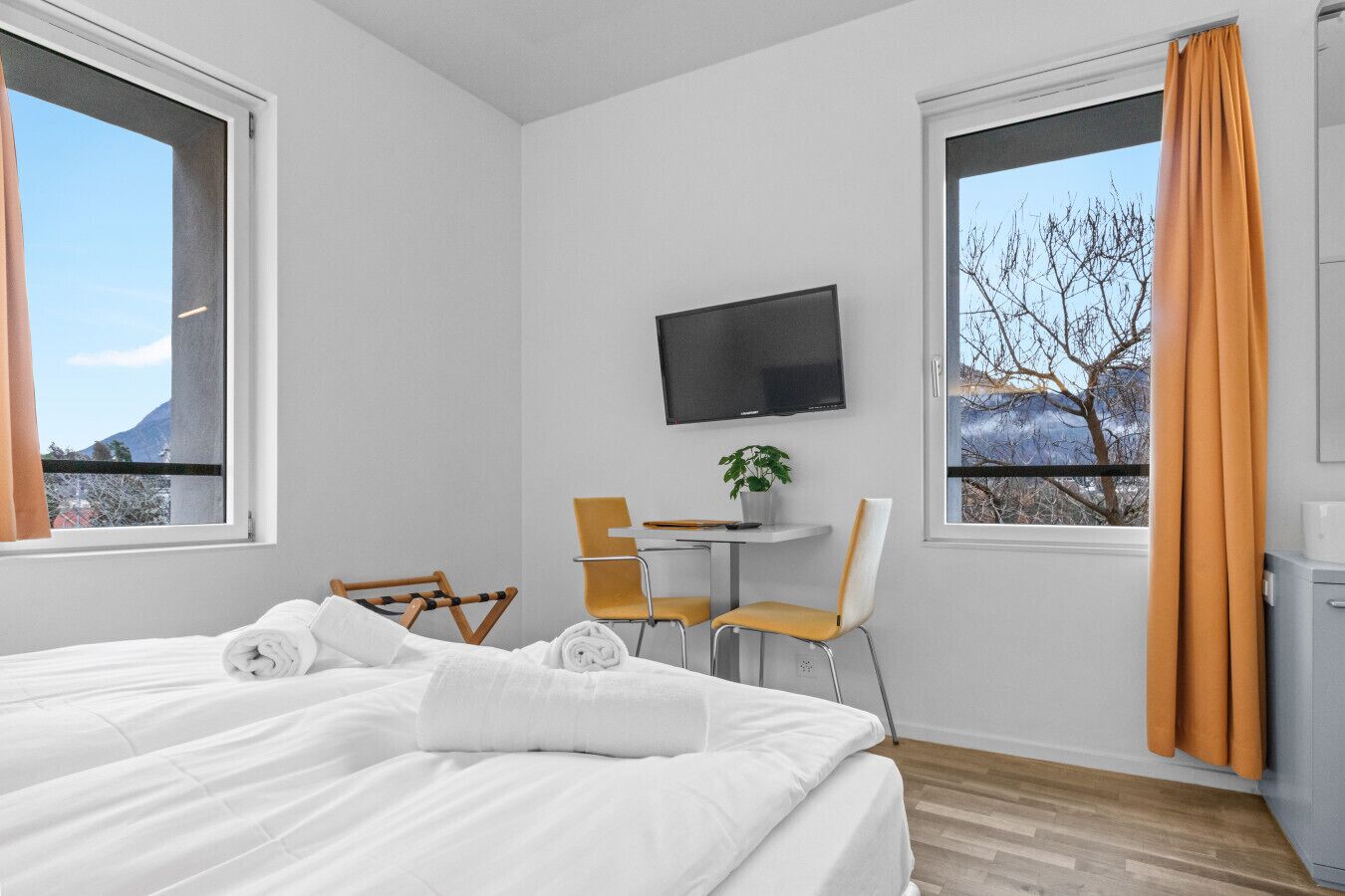 Une chambre d’hôtel avec un lit, deux chaises, une petite table, un téléviseur et des fenêtres équipées de rideaux.