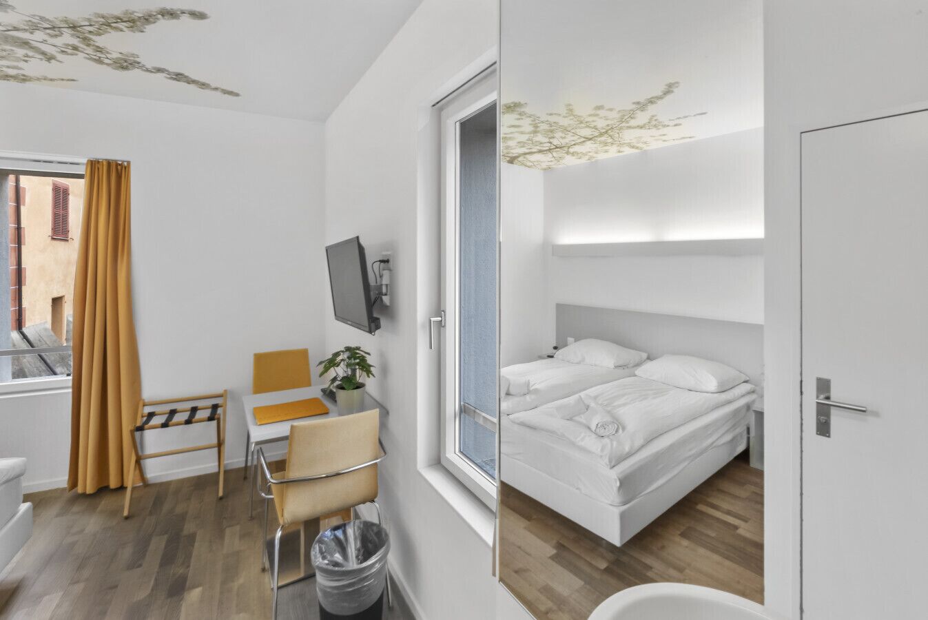 Una camera d'hotel moderna con un letto, una scrivania con una sedia, una televisione e una finestra con tende.