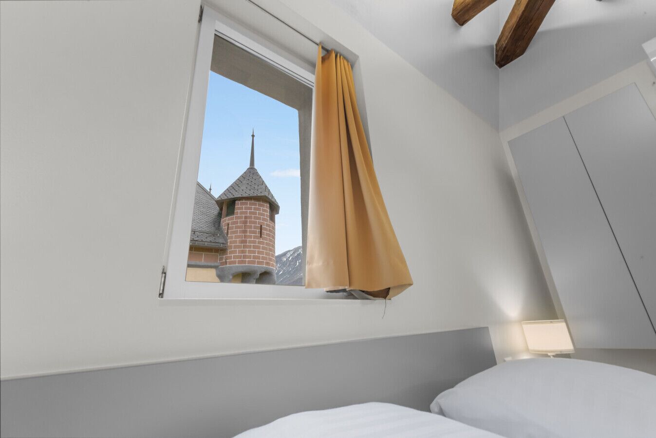 Un dormitorio con ventana, cama y vista a una torre de ladrillo.