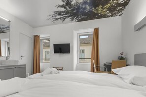 A modern hotel room with a large bed, a TV mounted on the wall, and a window with curtains. - Cozy twin room in the heart of Sierre (Sierre)