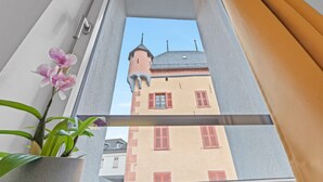A window with a view of a building with a tower and red shutters. - Cosy twin room in the heart of Sierre (Sierre)