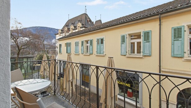 A balcony with a table and chairs, a building with green shutters, and a shop window with 'CAJONS' written on it. - Cosy twin room in the heart of Sierre (Sierre)