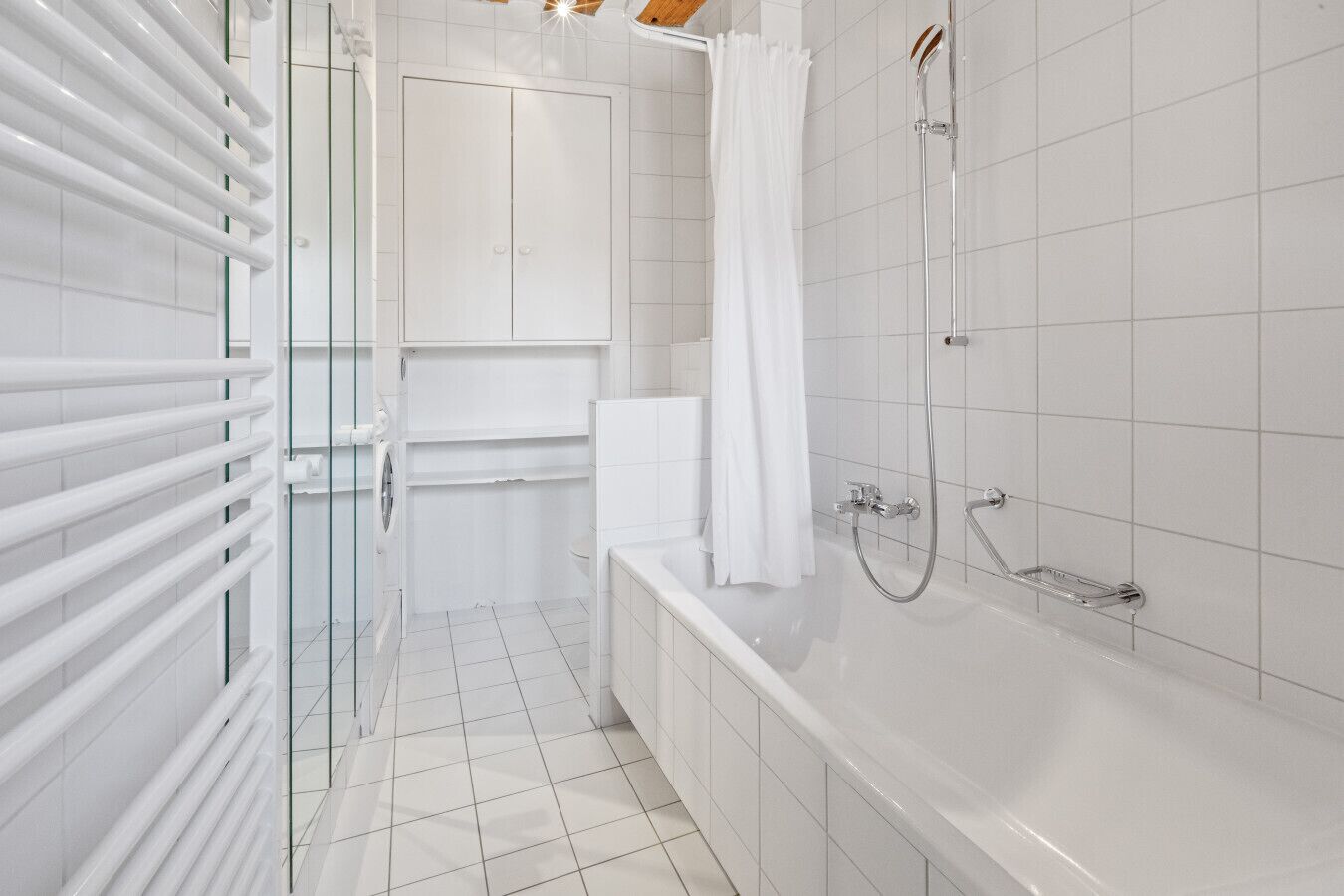 Een moderne badkamer met een douchecabine van glas, een witte badkuip en een glazen deur naar een toilet.