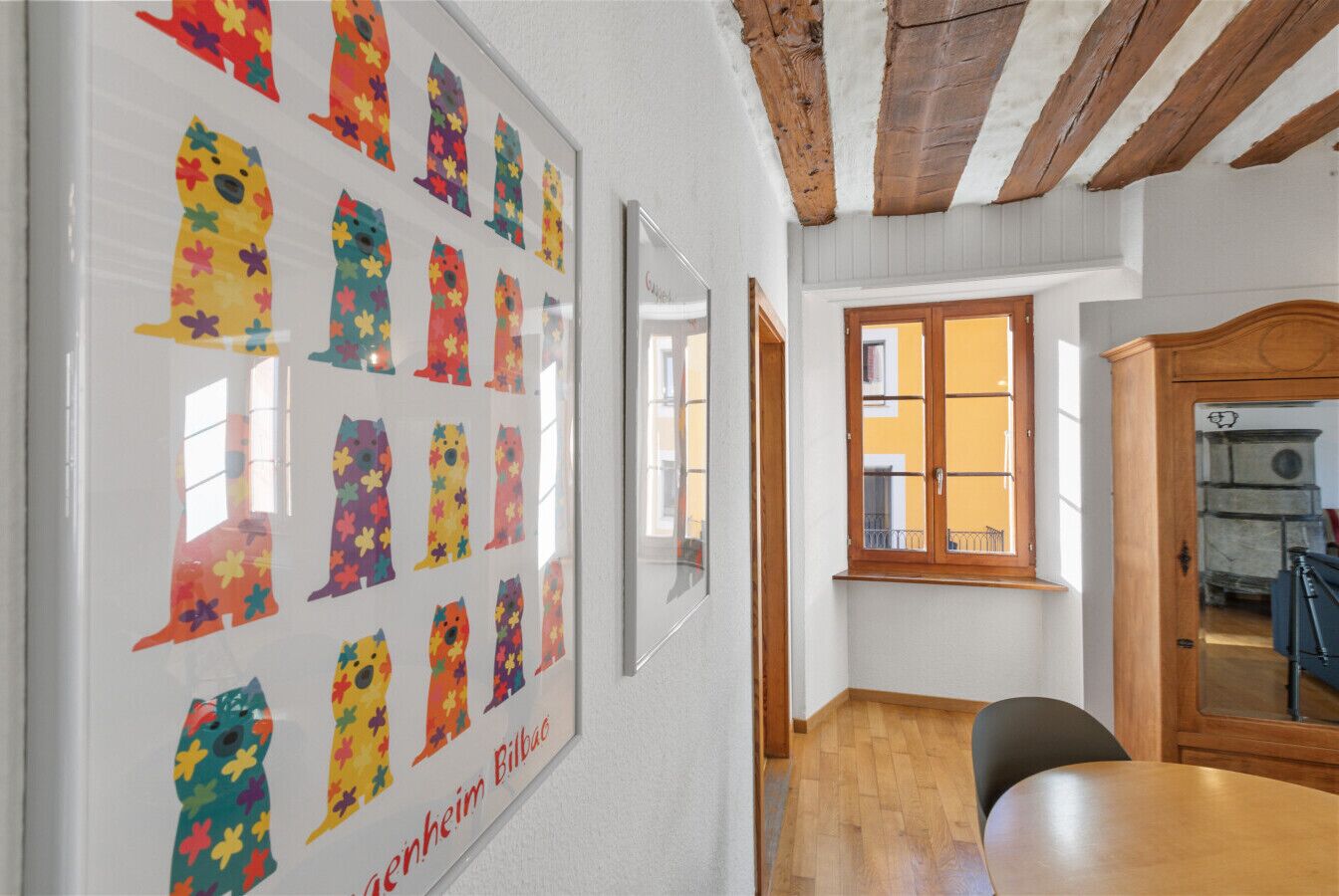 A hallway with framed artwork on the wall, a wooden table, and a window with a view of the outside.