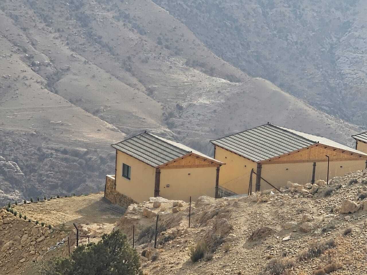 Una hilera de edificios sencillos de una sola planta con techos planos, ubicados en una ladera con un paisaje árido al fondo.