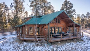 Eine Blockhütte mit Veranda und Sitzbereich im Freien, umgeben von einem weißen Zaun und schneebedecktem Gelände.
