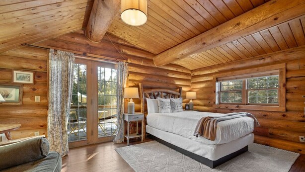 Ein Schlafzimmer in einer Blockhütte mit einem Bett, Nachttischen und Blick ins Freie.