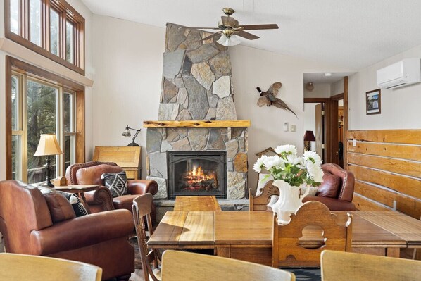 A cozy living room with a stone fireplace, leather furniture, and a ceiling fan.