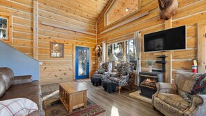 Ein gemütliches Blockhaus-Interieur mit Kamin, Ledersofas, gemusterten Sesseln und einem Fernseher.