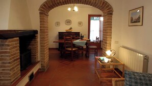 A dining area with a brick fireplace, a table set for four, and a chair with a lamp. - Comiti Farmhouse - David Apartment (Montaione)