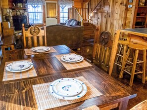 A wooden dining table set with plates and placemats, a bar stool, and a staircase leading to a lofted area. - Golden Trout-2 bedroom/Hot Tub/Location (Broken Bow)