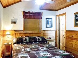 A cozy bedroom with a wooden ceiling, a bed with a quilt, a bedside lamp, a window with blinds, and a framed picture on the wall. - Golden Trout-2 bedroom/Hot Tub/Location (Broken Bow)