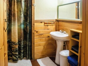 A wooden cabin bathroom with a white sink, wooden shelves, a mirror, and a shower curtain. - Golden Trout-2 bedroom/Hot Tub/Location (Broken Bow)