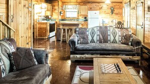 A wooden cabin interior with a living area featuring two sofas, a coffee table, and a kitchen in the background. - Golden Trout-2 bedroom/Hot Tub/Location (Broken Bow)