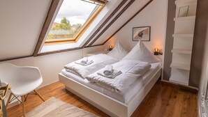 Une chambre avec un puits de lumière, un lit avec du linge de lit blanc, une chaise blanche et un plancher en bois.
