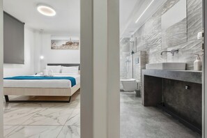 Un dormitorio moderno con cama, mesita de noche y un cuadro en la pared. El baño cuenta con bañera, lavabo y espejo.