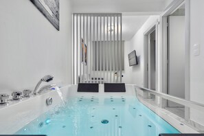 Un baño moderno con una bañera jacuzzi de vidrio, zona de ducha y un inodoro.
