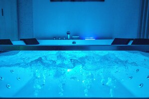 Un jacuzzi grande y rectangular con zona de estar integrada y un moderno grifo.