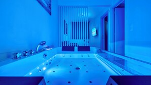 A modern bathroom with a large bathtub, a wall-mounted TV, and a ceiling light. - Premium Jacuzzi Suite at the City Center (Thessaloniki)