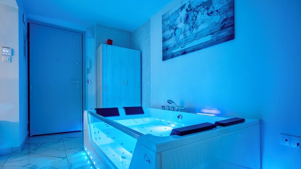 A modern bathroom with a large bathtub, a door, and a wall-mounted artwork. - Premium Jacuzzi Suite at the City Center (Thessaloniki)