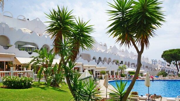 Et resort med pool, palmer og hvide bygninger med buer.