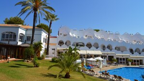 Et resort med swimmingpool, palmer og en hvid bygning med buede vinduer.