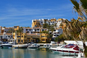 Boats docked in a tranquil marina surrounded by Mediterranean-style buildings with balconies and flat roofs.