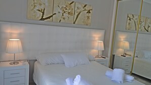 Et hotelværelse med en stor seng, to sengeborde med lamper, et spejl og kunst på væggen.