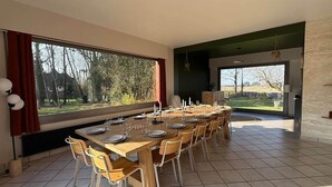 A dining area with a large table set for six, large windows with curtains, and a view of trees and a house outside. - The Saint-Josse Tribe (Saint-Josse)