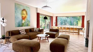 A modern living room with a sectional sofa, ottomans, a coffee table, and a dining area with a long table and chairs. - The Saint-Josse Tribe (Saint-Josse)